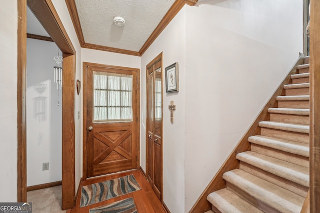 doorway with crown molding, light hardwood / wood-style flooring, and a textured ceiling