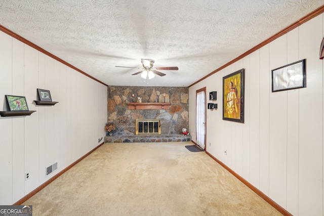 unfurnished living room featuring a stone fireplace, ceiling fan, crown molding, and carpet