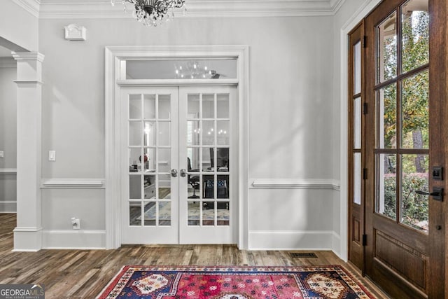 foyer entrance with french doors, decorative columns, hardwood / wood-style floors, a chandelier, and ornamental molding