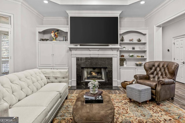 living room featuring a fireplace, hardwood / wood-style flooring, crown molding, and built in features