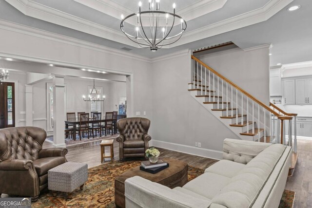 living room featuring ornamental molding, a notable chandelier, dark wood-type flooring, and a tray ceiling