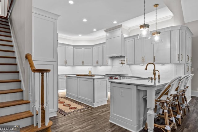 kitchen with light stone countertops, sink, dark wood-type flooring, pendant lighting, and a kitchen island with sink