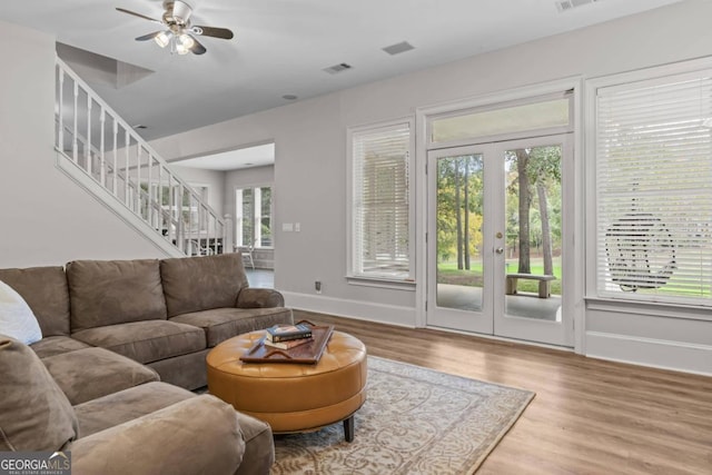 living room with a wealth of natural light, light hardwood / wood-style flooring, ceiling fan, and french doors