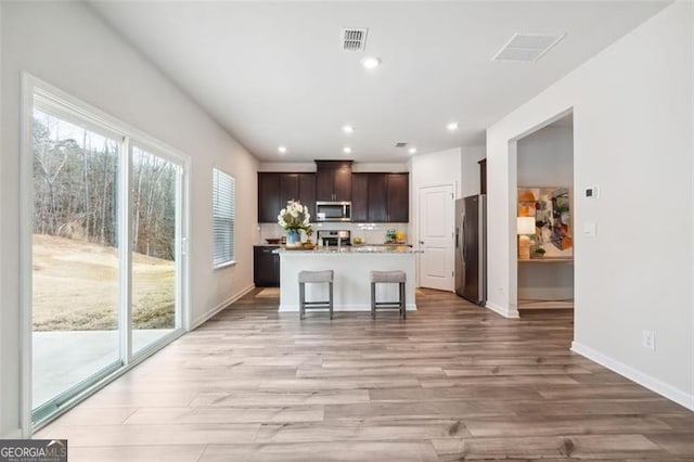 kitchen with a kitchen breakfast bar, light wood-type flooring, dark brown cabinetry, stainless steel appliances, and an island with sink