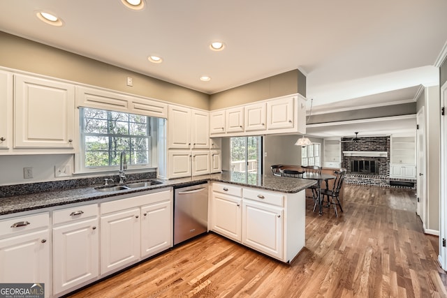 kitchen featuring white cabinetry, sink, a brick fireplace, stainless steel dishwasher, and kitchen peninsula