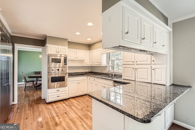 kitchen featuring ornamental molding, white cabinetry, sink, kitchen peninsula, and light wood-type flooring