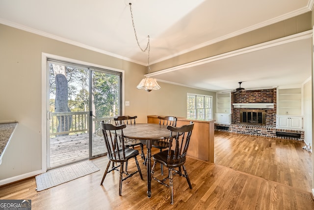 dining area featuring ceiling fan, hardwood / wood-style floors, ornamental molding, and a brick fireplace