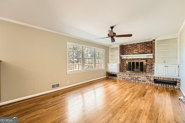 unfurnished living room featuring built in features, a fireplace, hardwood / wood-style floors, crown molding, and ceiling fan