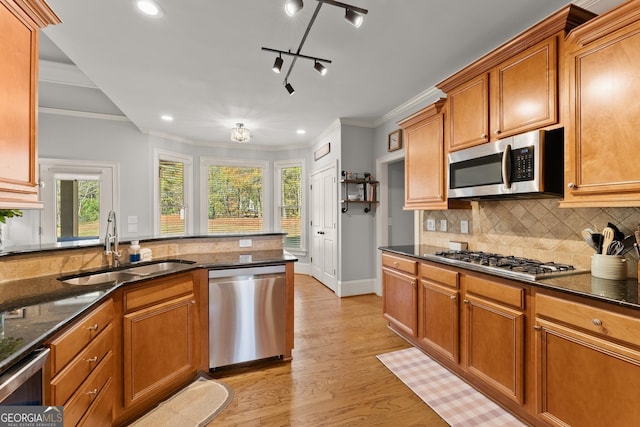 kitchen featuring sink, dark stone countertops, light hardwood / wood-style floors, appliances with stainless steel finishes, and ornamental molding