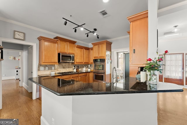 kitchen with kitchen peninsula, appliances with stainless steel finishes, light wood-type flooring, ornamental molding, and dark stone countertops