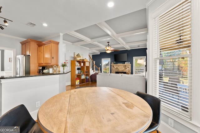 dining area with coffered ceiling, a stone fireplace, ceiling fan, light wood-type flooring, and beamed ceiling