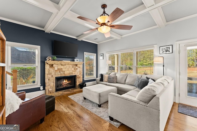 living room with beam ceiling, a stone fireplace, light wood-type flooring, and coffered ceiling