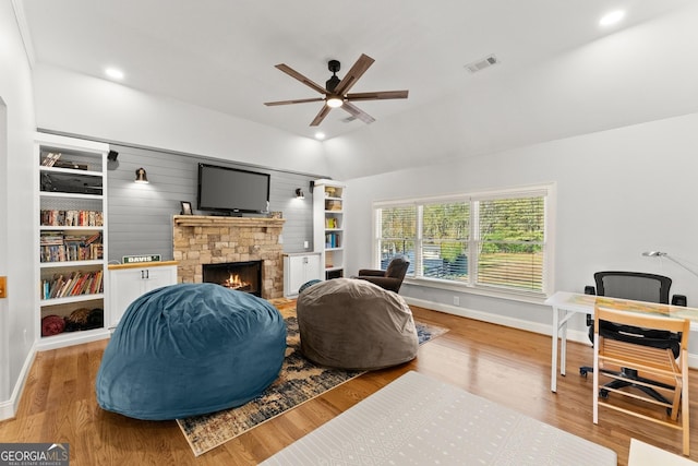 living room with a stone fireplace, ceiling fan, light hardwood / wood-style floors, and lofted ceiling