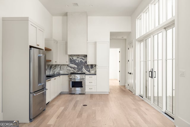 kitchen with white cabinetry, decorative backsplash, light hardwood / wood-style floors, and premium appliances