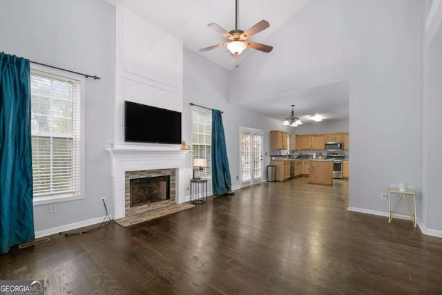 unfurnished living room featuring ceiling fan with notable chandelier, a wealth of natural light, high vaulted ceiling, and dark wood-type flooring