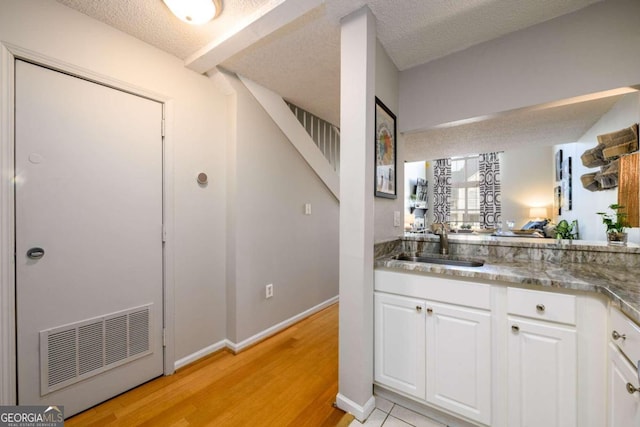 kitchen featuring dark stone counters, white cabinets, sink, a textured ceiling, and light hardwood / wood-style floors