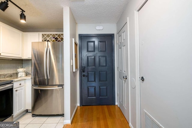 kitchen with appliances with stainless steel finishes, backsplash, a textured ceiling, light hardwood / wood-style floors, and white cabinetry