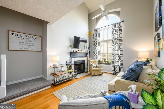 living room featuring hardwood / wood-style floors, a tile fireplace, vaulted ceiling, ceiling fan, and a textured ceiling