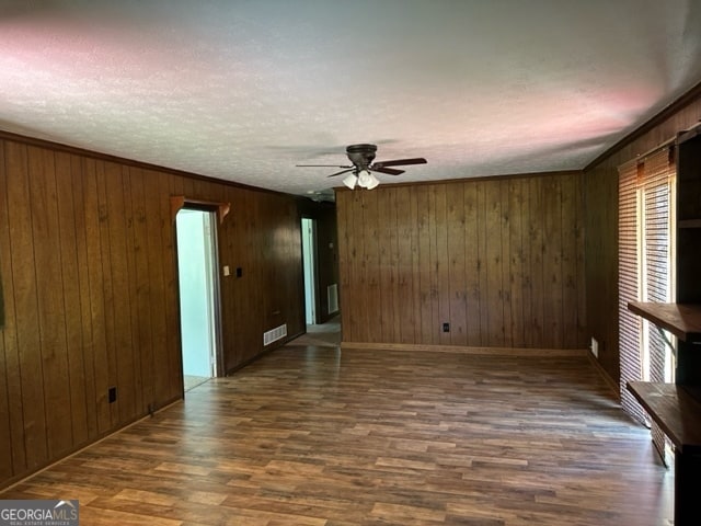 unfurnished room featuring ornamental molding, wooden walls, ceiling fan, and dark wood-type flooring