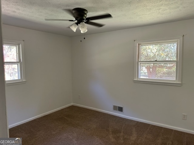 spare room featuring dark colored carpet, a textured ceiling, ceiling fan, and a healthy amount of sunlight