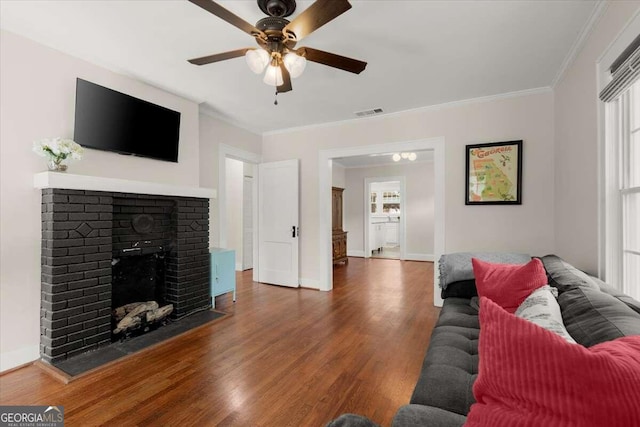 living room with a brick fireplace, ceiling fan, dark wood-type flooring, and crown molding