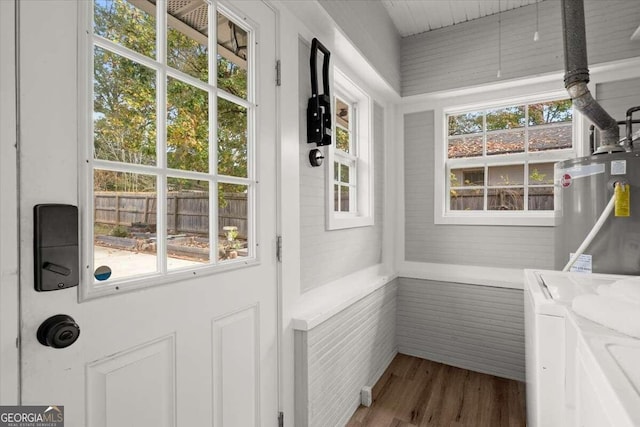 doorway with washing machine and clothes dryer, water heater, and hardwood / wood-style flooring