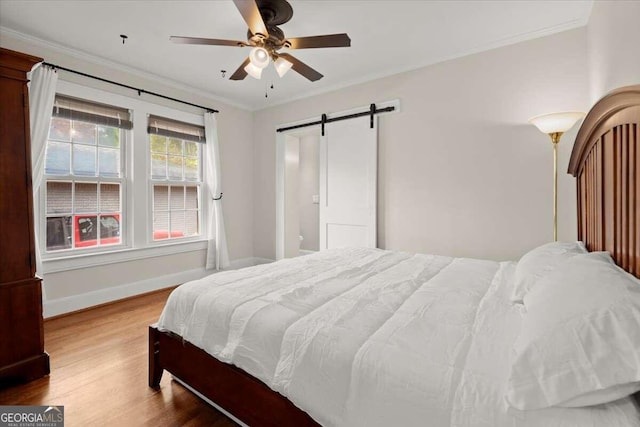 bedroom with a barn door, ceiling fan, hardwood / wood-style floors, and ornamental molding