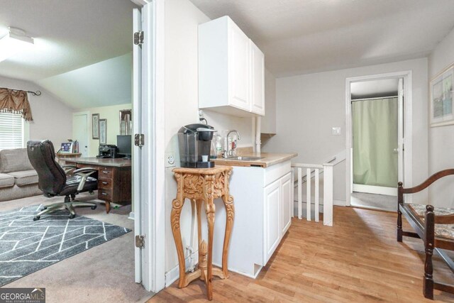 kitchen featuring lofted ceiling, white cabinets, sink, and light wood-type flooring