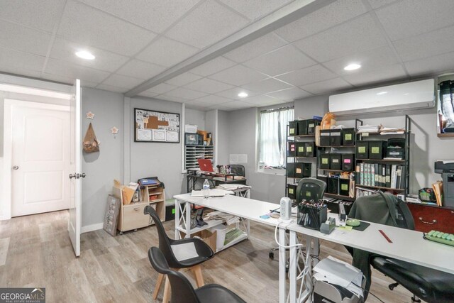 office area with an AC wall unit, a drop ceiling, and light wood-type flooring