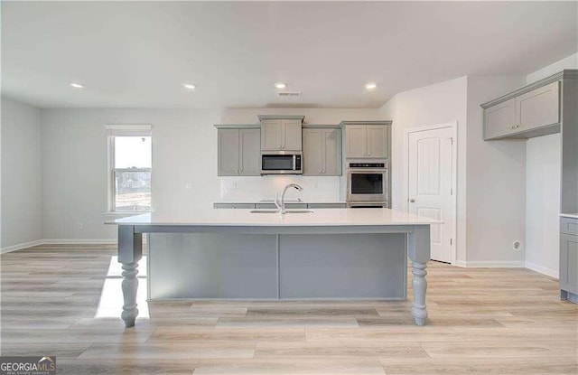 kitchen featuring gray cabinets, appliances with stainless steel finishes, and a kitchen island with sink