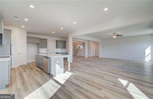 kitchen with a center island with sink, ceiling fan, light wood-type flooring, and stainless steel dishwasher