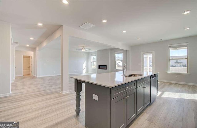 kitchen with sink, plenty of natural light, an island with sink, stainless steel dishwasher, and light hardwood / wood-style floors