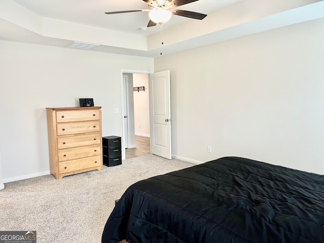 bedroom featuring light colored carpet, a raised ceiling, and ceiling fan