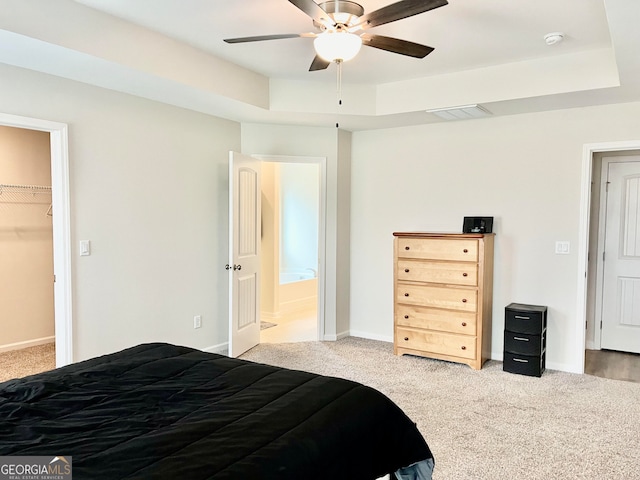 carpeted bedroom featuring a tray ceiling, a walk in closet, ceiling fan, and a closet