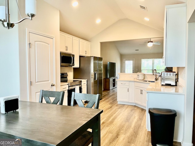 kitchen with sink, vaulted ceiling, decorative light fixtures, white cabinets, and appliances with stainless steel finishes