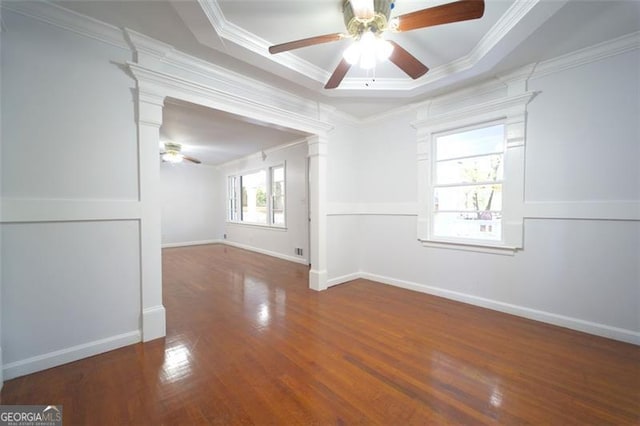 empty room featuring ornamental molding, dark wood-type flooring, ceiling fan, a raised ceiling, and decorative columns