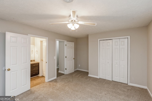 unfurnished bedroom featuring ensuite bathroom, a closet, light colored carpet, a textured ceiling, and ceiling fan