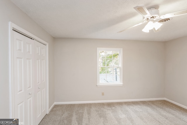 unfurnished bedroom with ceiling fan, a closet, light carpet, and a textured ceiling