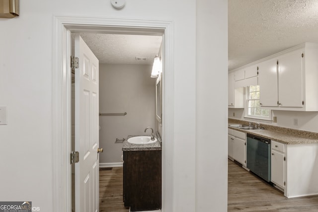 kitchen featuring white cabinetry, sink, stainless steel dishwasher, a textured ceiling, and light wood-type flooring