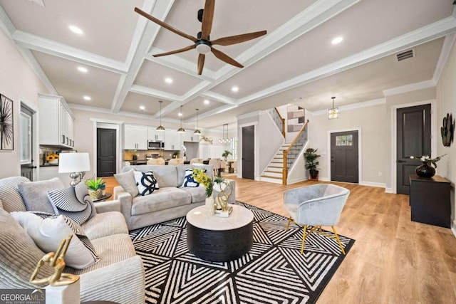 living room featuring light hardwood / wood-style flooring, beam ceiling, coffered ceiling, crown molding, and ceiling fan with notable chandelier