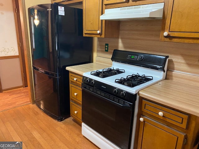 kitchen with black fridge, white range with gas stovetop, and light hardwood / wood-style floors