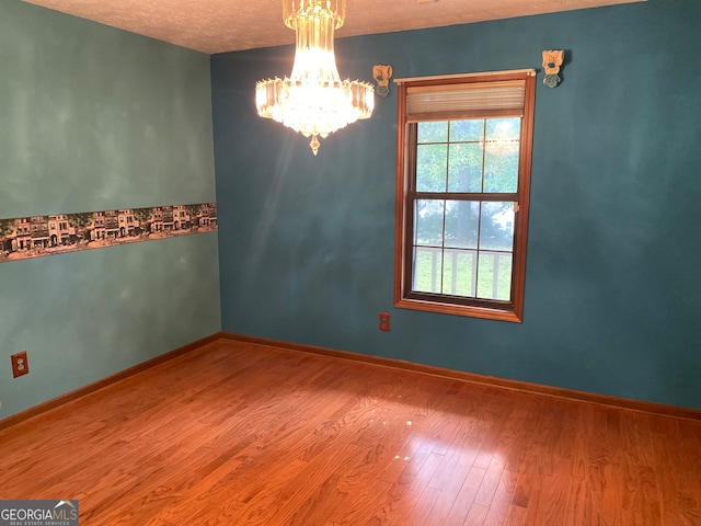 empty room with a chandelier, hardwood / wood-style floors, and a textured ceiling