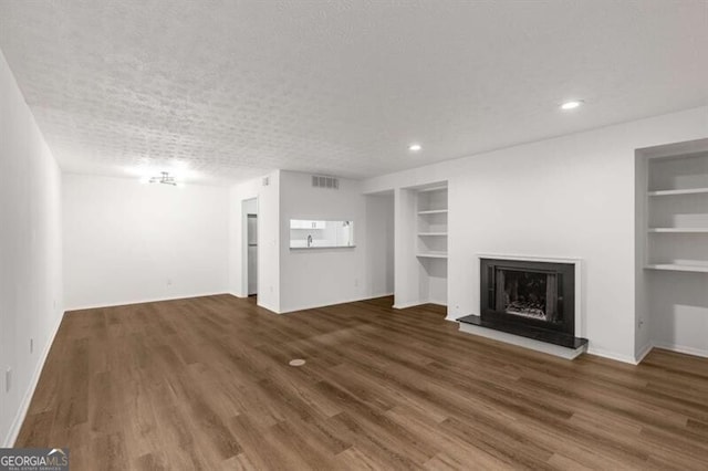 unfurnished living room with built in shelves, a textured ceiling, and dark hardwood / wood-style floors