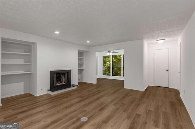 unfurnished living room featuring built in shelves, ceiling fan, dark hardwood / wood-style floors, and a textured ceiling