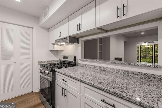 kitchen with gas stove, white cabinets, wood-type flooring, and light stone countertops