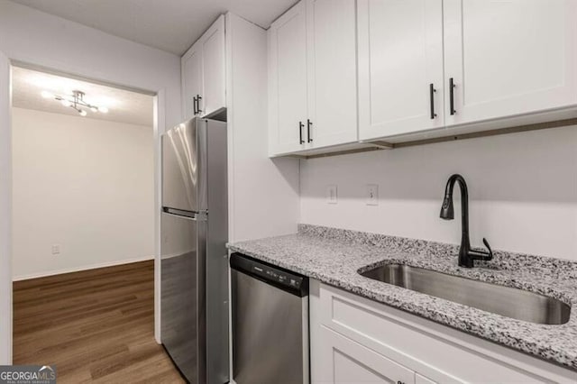 kitchen featuring light stone countertops, stainless steel appliances, sink, wood-type flooring, and white cabinets