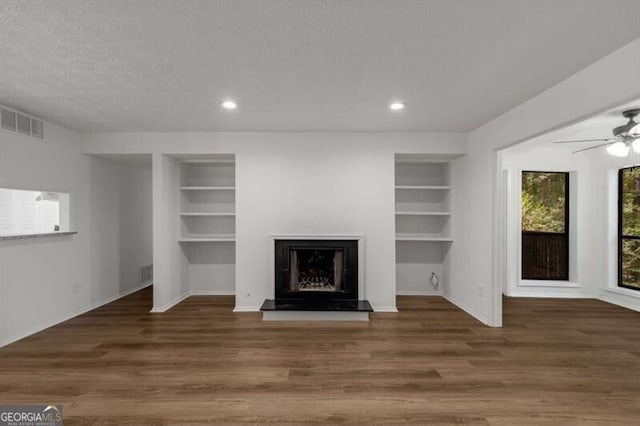 unfurnished living room with a textured ceiling, dark hardwood / wood-style floors, built in features, and ceiling fan