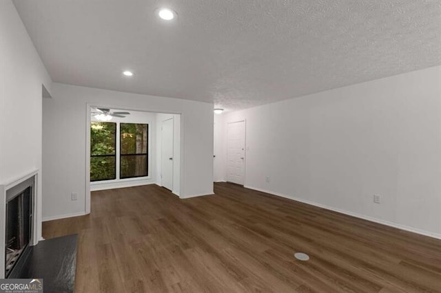 unfurnished living room with ceiling fan, dark hardwood / wood-style flooring, and a textured ceiling