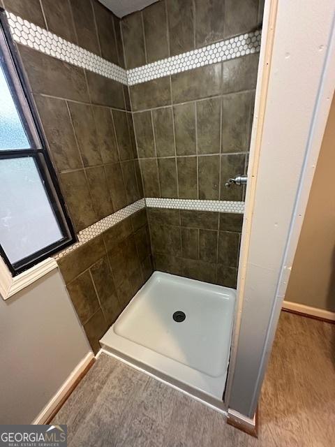 bathroom with a tile shower and wood-type flooring