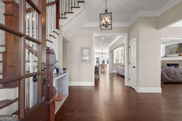 foyer with a stone fireplace, dark wood-type flooring, crown molding, and a chandelier